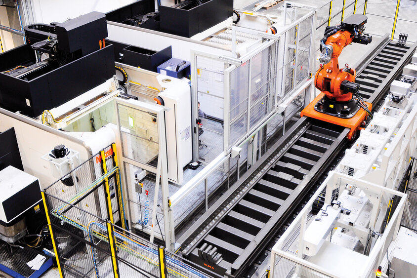 Foto einer Multi-Maschinen-Automatisierungsanlage, die einen Transferroboter zeigt, der zwischen zwei Bearbeitungszentren operiert. Die Aufnahme verdeutlicht die komplexe und effiziente Zusammenarbeit der Maschinen, die durch den zentralen Roboterarm ermöglicht wird, um präzise und schnelle Fertigungsprozesse zu gewährleisten.
