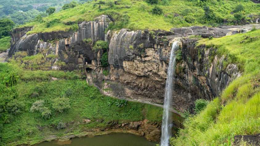 Ein beeindruckender Wasserfall stürzt von einer steilen Klippe in ein ruhiges Becken, umgeben von üppigem Grün und felsigen Formationen.