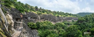 Eine beeindruckende Reihe von Höhlen, in Fels gemeißelt, eingebettet in eine grüne Hügellandschaft, mit Zugangswegen, die durch die steilen Klippen führen.