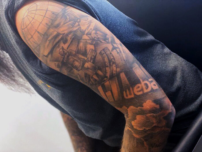 An upper arm tattoo of a weba Werkzeugbau employee. The tattoo features the weba logo along with various technical elements such as gears, machines, and a globe. It symbolizes the employee's passion for the company and his identification with weba's technology and values.