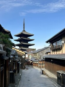 A traditional Japanese street with wooden houses and an impressive pagoda in the background under a blue sky.