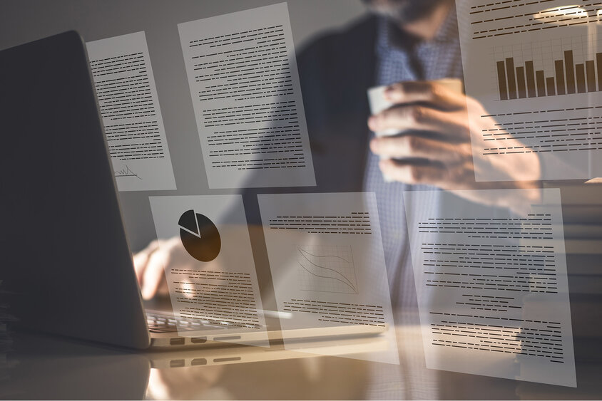 Ein Geschäftsmann sitzt vor einem offenen Laptop, während das Bild von digitalen Dokumenten überlagert wird, die Grafiken und Texte zeigen.
