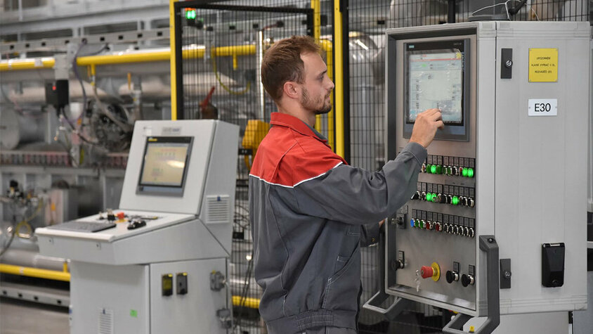 Ein konzentrierter Maschinenbediener der weba Werkzeugbau steht an der komplexen Steuerungskonsole der Warmformlinie, umgeben von leuchtenden Displays und Bedienelementen.