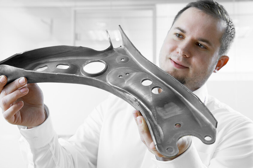 A quality manager inspects the quality of a hot-formed control arm after series production.