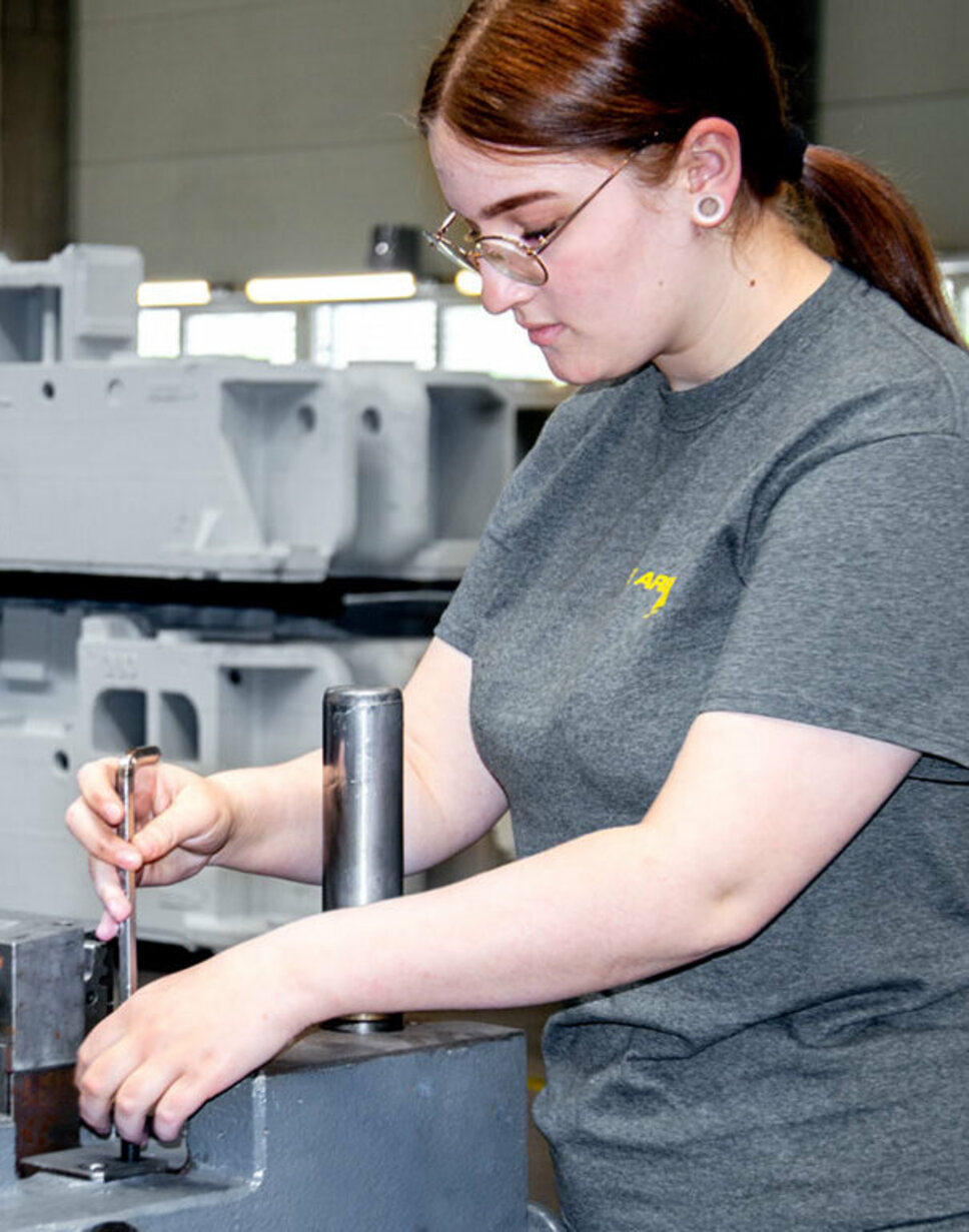 Eine junge Werkzeugbautechnikerin montiert Stanzwerkzeuge.