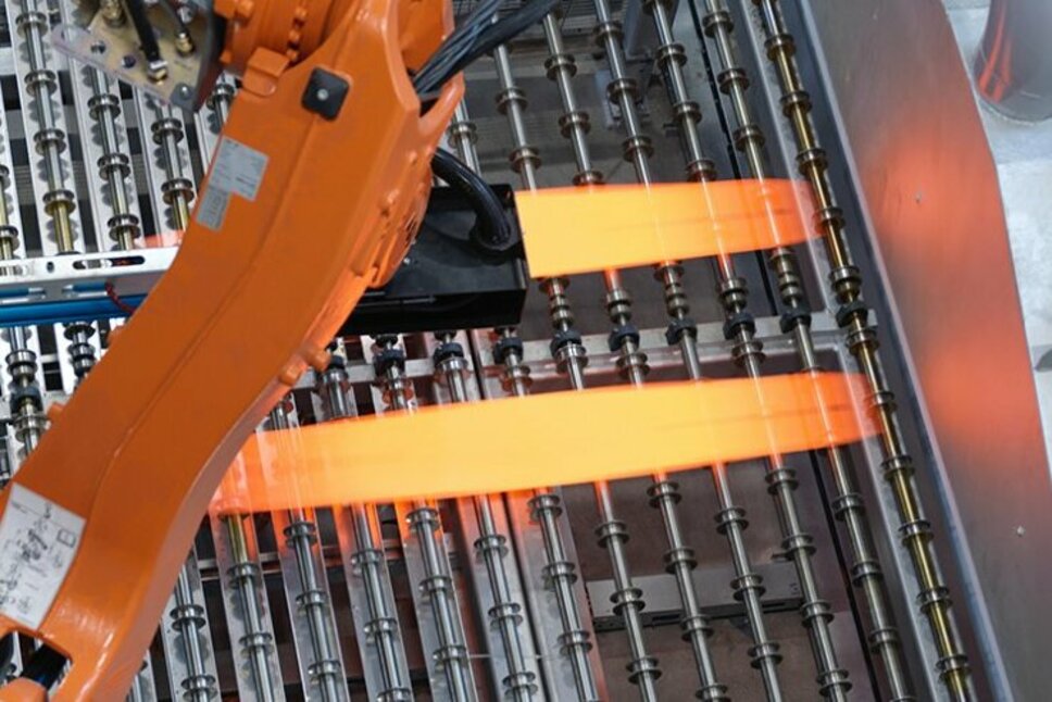 An industrial robotic arm positioned in process technology is placing glowing hot metal sheets onto a production line. The use of state-of-the-art technology optimizes the press hardening process and ensures precise control of the forming processes at weba Werkzeugbau.