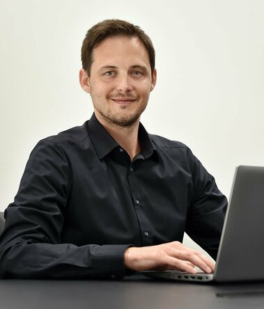 Ondrej Zima, Human Resource Manager der weba Olomouc sitzt avor einem geöffneten Laptop und  lächelt in die Kamera