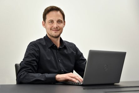 Ondrej Zima, Human Resource Manager der weba Olomouc sitzt avor einem geöffneten Laptop und  lächelt in die Kamera