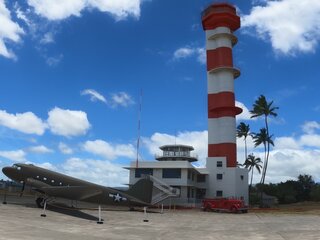 A distinctive red and white control tower in Pearl Harbor, Hawaii, with a historic military aircraft in the foreground.