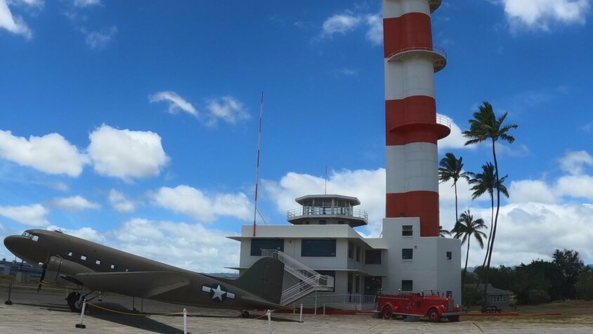 Ein markanter rot-weißer Kontrollturm in Pearl Harbor, Hawaii, mit einem historischen Militärflugzeug im Vordergrund.